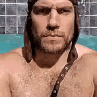 a shirtless man with a beard and a hat is sitting in a pool .