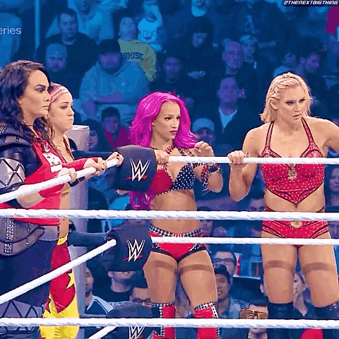 three women are standing in a wrestling ring holding ropes and one has a w on her hat .