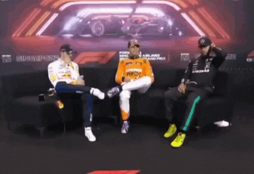 three men are sitting on a couch in front of a sign that says singapore on it