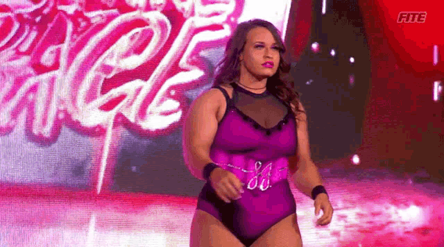 a woman in a purple swimsuit is walking on a stage in front of a large screen .