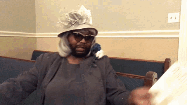 a woman wearing a hat and sunglasses is sitting on a bench