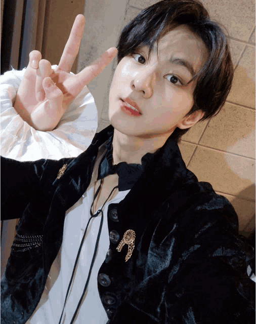 a young man wearing a black jacket and a white shirt is giving a peace sign