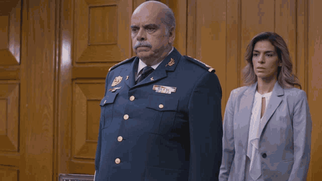 a man in a military uniform salutes while a woman in a suit looks on