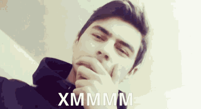 a man covering his mouth with his hand and the words xmmmm written on the bottom right