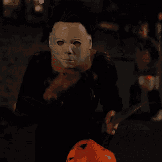 a person wearing a mask is holding a pumpkin and a knife