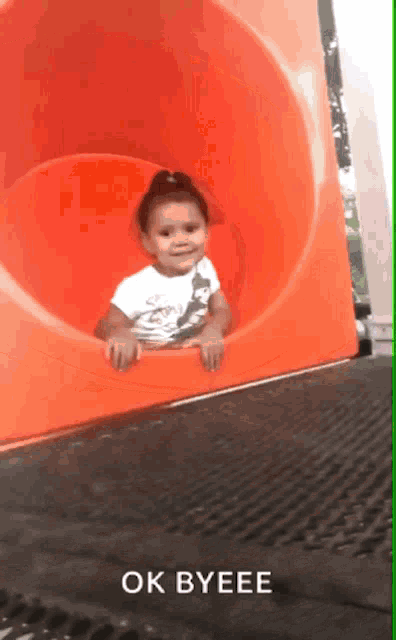 a little girl is going down an orange slide with the words ok byeee above her