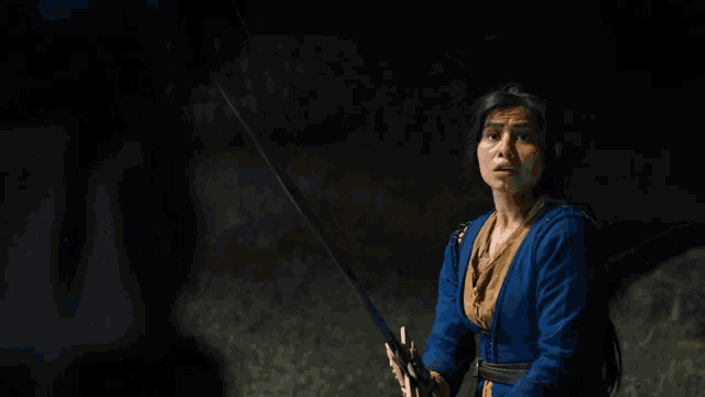 a woman in a blue dress is holding a sword in a field at night