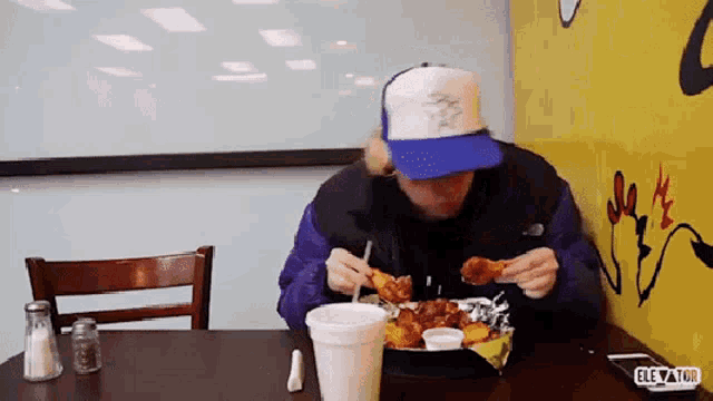 a man wearing a blue hat is eating chicken wings at a restaurant called the elevator
