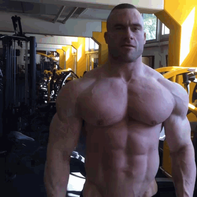 a man without a shirt is standing in a gym with a yellow machine