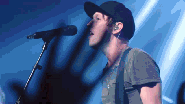 a man singing into a microphone while wearing a baseball cap