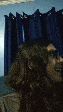 a woman with long hair and glasses is smiling in front of blue curtains