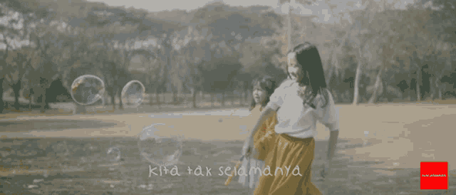 a girl in a yellow skirt is playing with soap bubbles in a field with the words kita tak selamanya above her