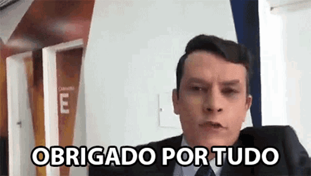 a man in a suit and tie is making a funny face and saying obrigado por tudo .