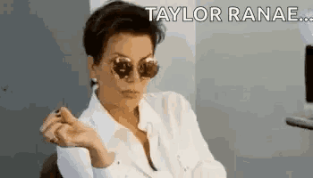 a woman wearing sunglasses and a white shirt is sitting in a chair and making a funny face .