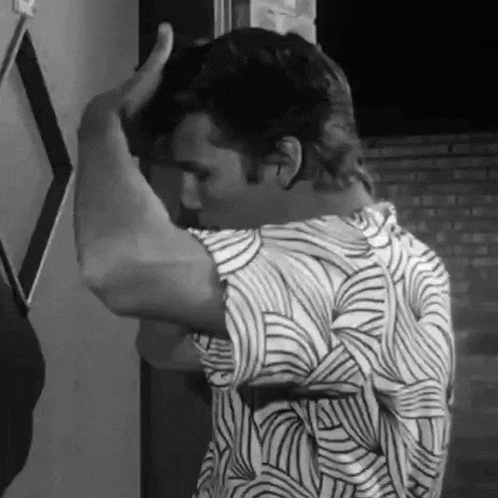 a black and white photo of a man in a striped shirt standing in front of a door .