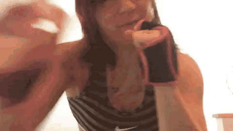 a woman wearing boxing gloves is holding a bottle of wine in her hand .