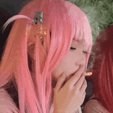 a woman wearing a pink wig is smoking a cigarette .