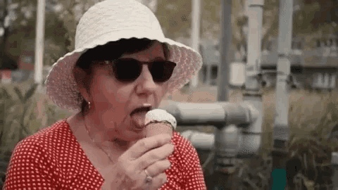 a woman wearing a hat and sunglasses is eating ice cream .