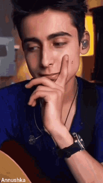 a young man is sitting at a table with his hand to his chin .