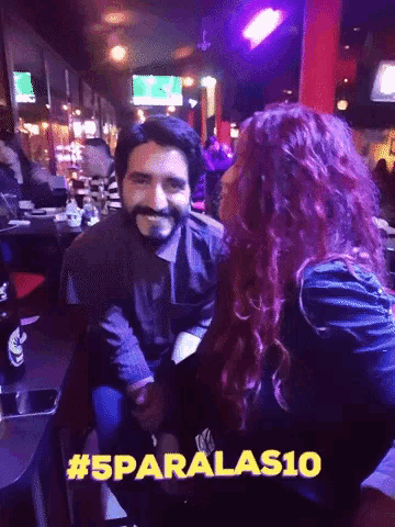a man and a woman are sitting at a table with # 5paralas10 on the bottom right