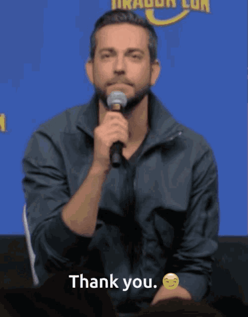 a man holding a microphone says thank you in front of a blue background