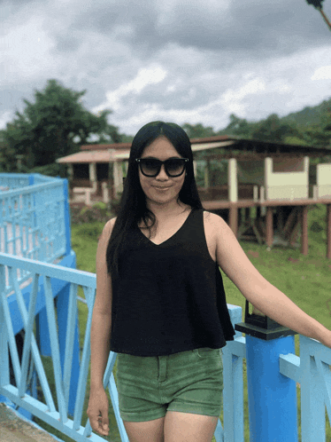 a woman wearing sunglasses and a black tank top stands on a blue railing