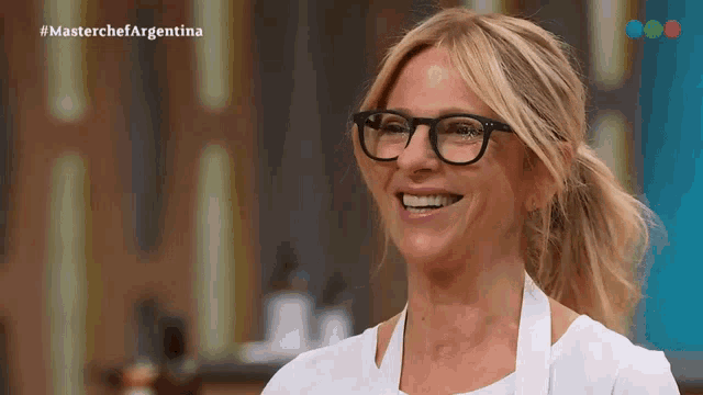 a woman wearing glasses and a white apron is smiling in front of a masterchef argentina logo