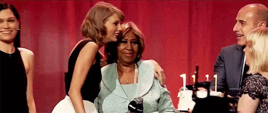 a woman is kissing an older woman on the cheek while a group of people are standing around her .