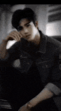 a young man in a denim jacket is sitting down with his hand on his face .