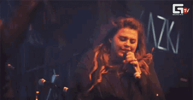 a woman singing into a microphone with the letters gtv in the background