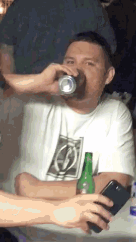 a man is drinking from a can while holding a green bottle
