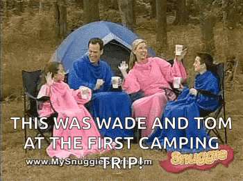 a family is sitting in front of a tent wearing blankets while camping .