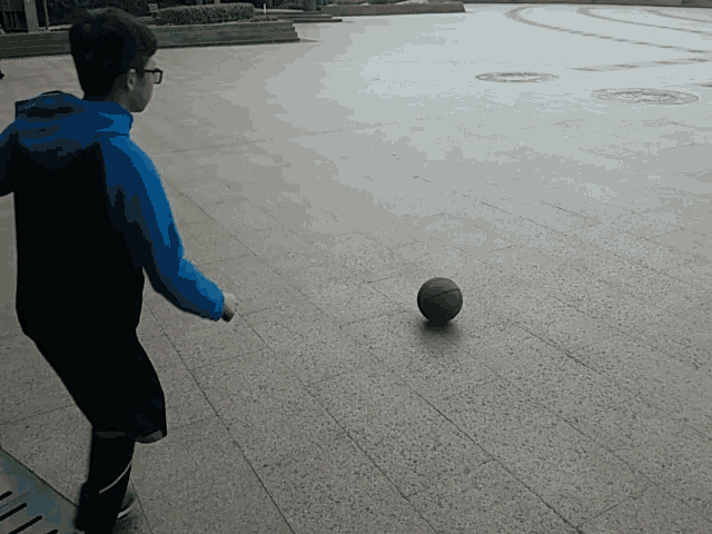 a boy in a blue hoodie is kicking a basketball on the ground