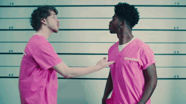 a man in a pink shirt with a tattoo on his neck stands next to another man in a pink shirt