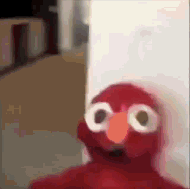 elmo from sesame street is standing in front of a white wall .