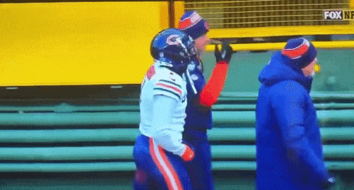 a football player is being helped off the field by a man in a blue jacket .