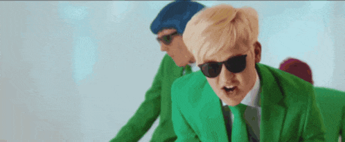 a man in a green suit and sunglasses is standing next to another man in a blue hat