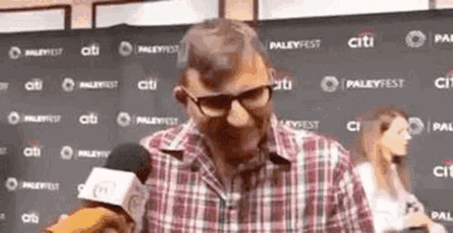 a man in a plaid shirt is talking into a microphone at a press conference .