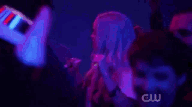 a woman is singing into a microphone in front of a crowd of people in a dark room .