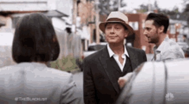 a man in a suit and hat is shaking hands with a woman in a grey suit .