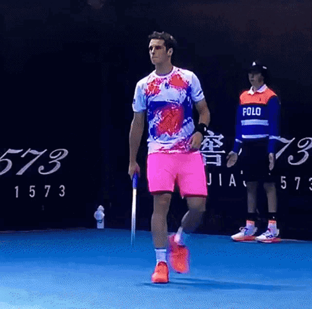 a man wearing a polo shirt is walking on a blue court