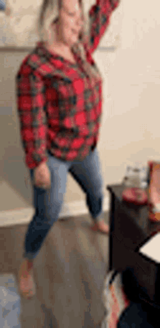 a woman in a plaid shirt and blue jeans is standing on one leg in a living room .