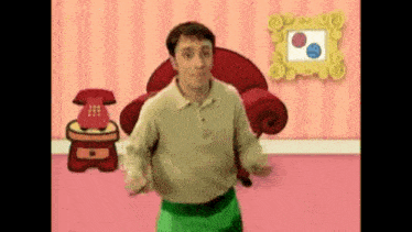 a man in a green skirt is dancing in a room with a red chair and a telephone .