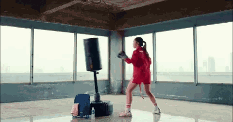 a woman in a red shirt is boxing in an empty room
