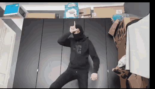 a man wearing a black hoodie and a mask is dancing in front of a closet .
