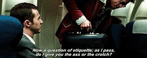 a man in a suit is talking to another man on an airplane while holding a briefcase