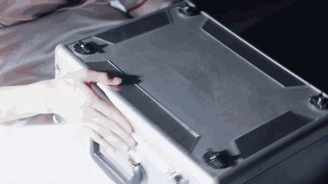 a person 's hand is on the bottom of a metal briefcase
