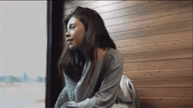 a woman in a grey sweater looks out a window