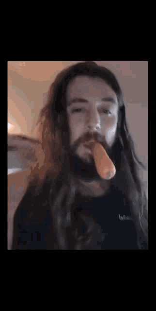 a man with long hair and a beard is chewing on a carrot