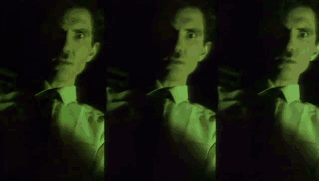 a man in a suit and tie is standing in the dark with a green light shining on his face .